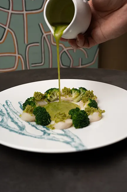 Capesante gratinate con prezzemolo e broccoli con salsa al prezzemolo versata al tavolo, ristorante di pesce Da Sacerno a Bologna