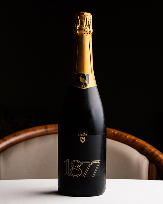 Bottiglia di spumante brut metodo classico da uve Pignoletto dell’Emilia-Romagna “1877” di Lodi Corazza (Valsamoggia), sul tavolo del ristorante Da Sacerno
